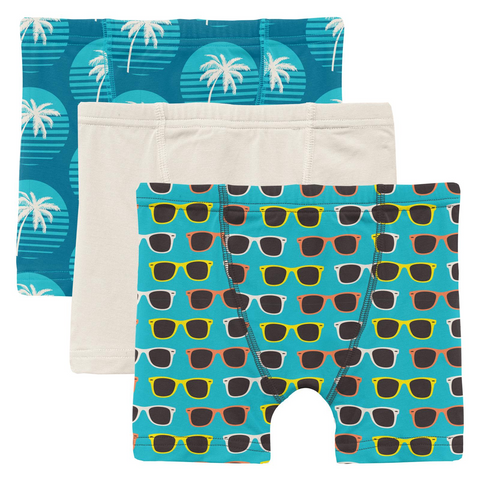 3 child boxer briefs. One is aqua with sunglasses all over it. One is solid natural color. One is Deep blue with aqua Sunset circles with white palm trees in them. 