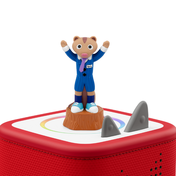 A small figurine of a bear-like character in a blue suit standing on a tree stump, placed on top of a red rounded rectangular base with gray shark-shaped elements, photographed on a clean white background.