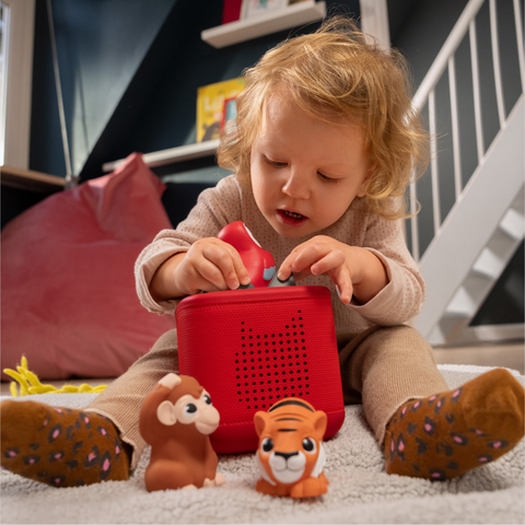 Child playing with a red toy box and animal figurines on a carpeted floor.