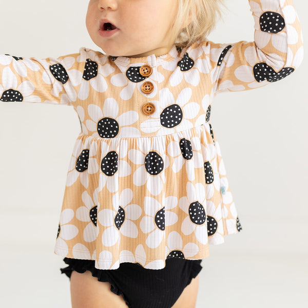 Girl wearing long sleeve henley with black bloomers. Top is sunflower print.