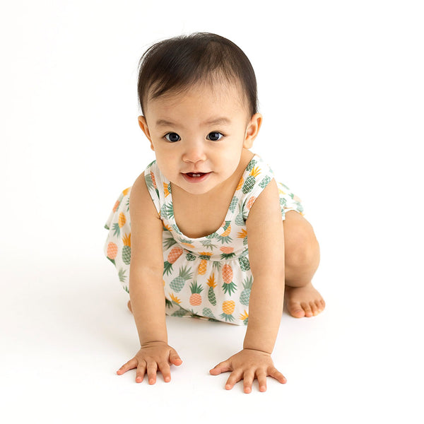 Child Crawling toward camera wearing Peplum top is sleeveless and has Pineapple print. Light Green, Dark green, Orange, and Yellow Pineapples are repeated all over gown. It comes with a pair of Bummies bottoms that have coordinating colors in stripes.