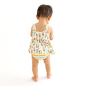 Child standing with their back to the camera wearing Peplum top is sleeveless and has Pineapple print. Light Green, Dark green, Orange, and Yellow Pineapples are repeated all over gown. It comes with a pair of Bummies bottoms that have coordinating colors in stripes.