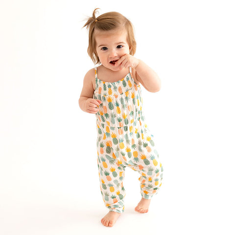 Toddler walking toward camera wearing Jumpsuit has a white background with Light Green, Dark Green, Yellow, and Orange Pineapples all over it.