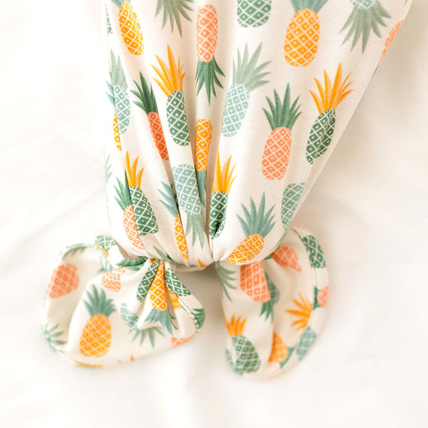 Bottom of knotted gown Pineapple print.  Light Green, Dark green, Orange, and Yellow Pineapples are repeated all over gown.