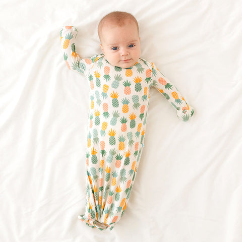 Baby wearing Pineapple print.  Light Green, Dark green, Orange, and Yellow Pineapples are repeated all over gown.
