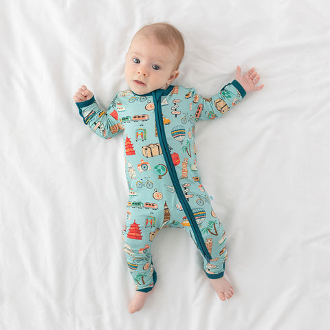 Baby wearing One Piece PJ with aqua canvas and iconic structures, buildings, and modes of transportation with a deep teal trim and cuffs
