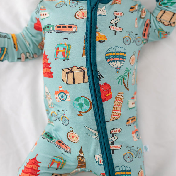 Close up of baby wearing One Piece PJ with aqua canvas and iconic structures, buildings, and modes of transportation with a deep teal trim and cuffs