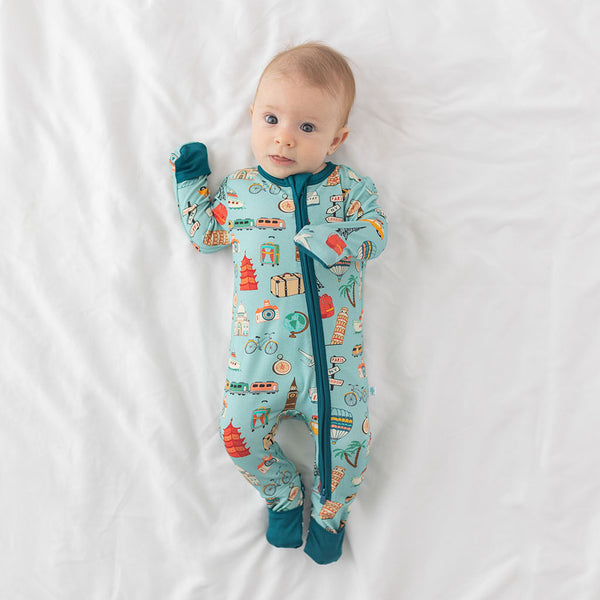 Baby wearing One Piece PJ with aqua canvas and iconic structures, buildings, and modes of transportation with a deep teal trim and cuffs