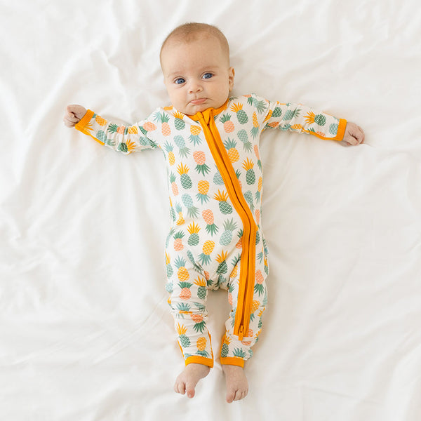 Baby wearing the One Piece. The Cuffs on arms and legs are open. This is the Pineapple print.  Light Green, Dark green, Orange, and Yellow Pineapples are repeated all over gown.