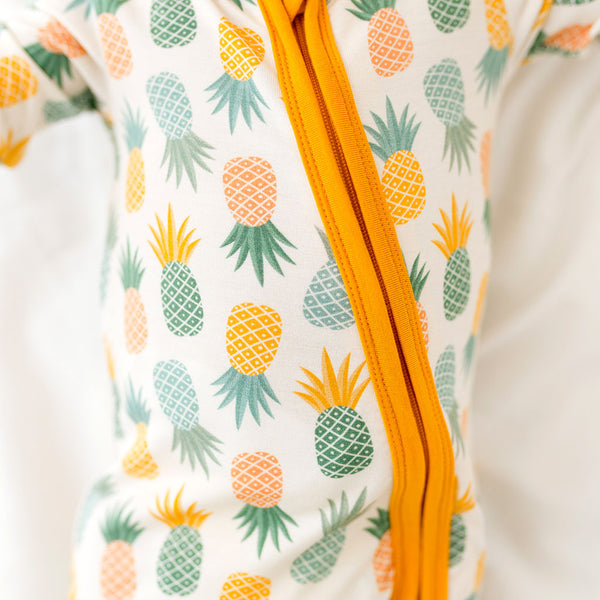 Close up of the Bright Orange Zipper Path on the Pineapple print.  Light Green, Dark green, Orange, and Yellow Pineapples are repeated all over gown.