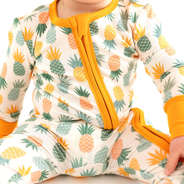 Close up shot of the toddler sitting in the Pineapple print.  Light Green, Dark green, Orange, and Yellow Pineapples are repeated all over gown.