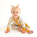 Toddler Sitting down in the One Piece. Pineapple print.  Light Green, Dark green, Orange, and Yellow Pineapples are repeated all over gown.