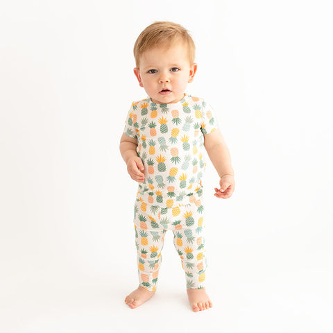 Toddler boy standing in the Pineapple print. Light Green, Dark green, Orange, and Yellow Pineapples are repeated all over.