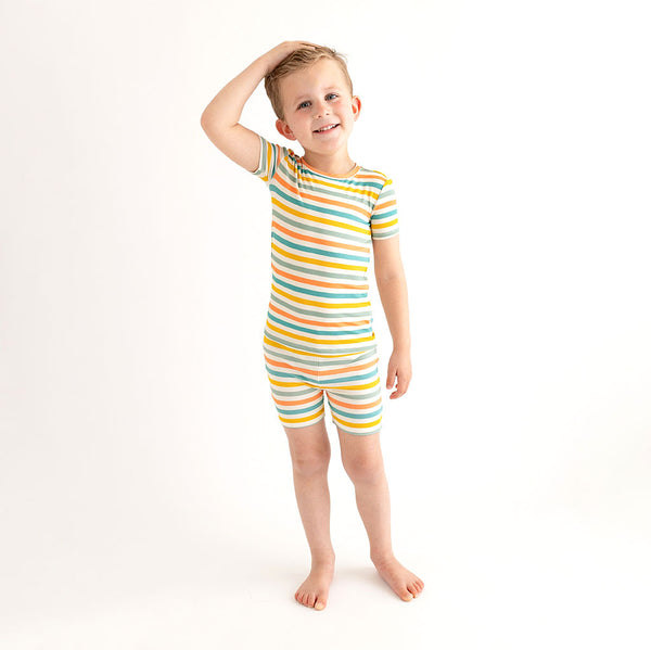 Boy wearing pajamas. These pajamas has a white background with horizontal stripes. Aqua, Mustard, Sage Green, and Coral