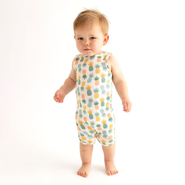 Boy standing in This print has a white background with Pineapple print. Light Green, Dark green, Orange, and Yellow Pineapples are repeated all over.