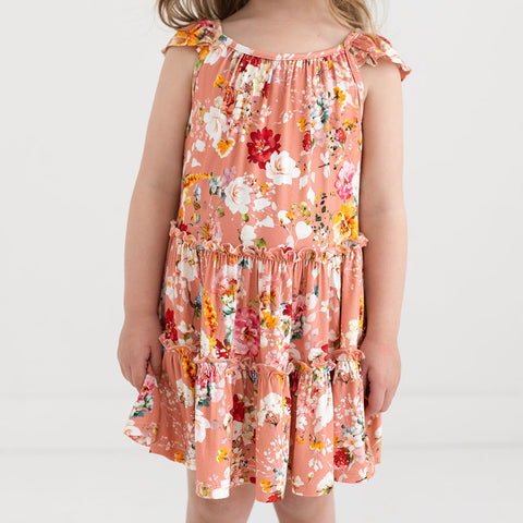 Girl in a tiered flutter sleeve dress. Print is orange, red, yellow and white floral on a peachy background.