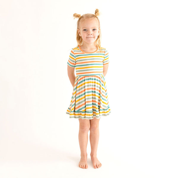 Girl wearing Short sleeve twirl has a scoop neckline. The print has a white background with horizontal stripes in aqua, sage green, mustard, and coral