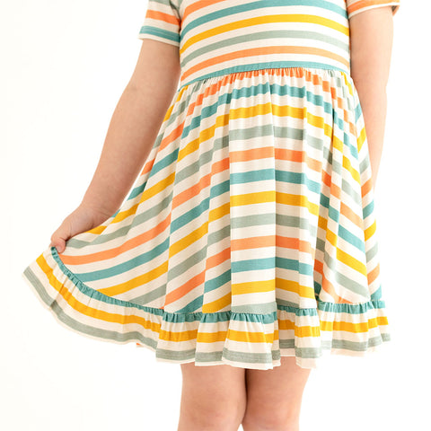 Close up shot of the bottom of twirl dress that Short sleeve twirl has a scoop neckline. The print has a white background with horizontal stripes in aqua, sage green, mustard, and coral