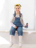 Girl holding Lottie Doll with Dark brown hair. in white leggings and jean skirt and red/white stripe shirt