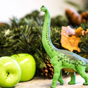 Green Brachiosaurus standing by two green apples