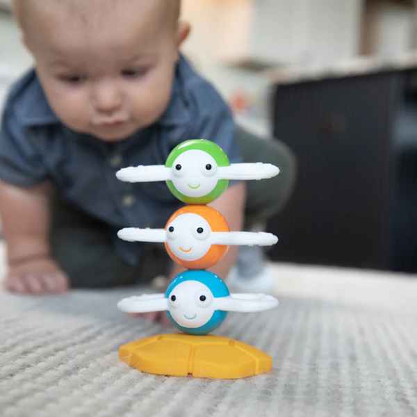 Baby in back ground crawling towards Blue, Orange, and green magnetic bee shaped toys