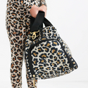 Girl holding Duffle bag with black straps and seams complete with gold hardware. The print is a Tan Leopard print