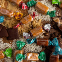 Assorted candies including caramels, toffees, and wrapped chocolates on a wooden surface.