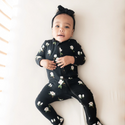 baby wearing footie pj's in An all-over floral print featuring small white magnolias with their leaves and stems contrasting vividly against a black background color called Midnight.