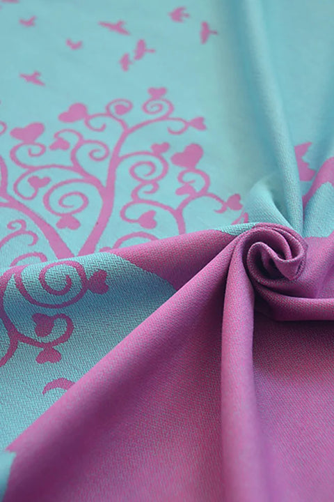 This is a KOKADI Flip Erna in Wonderland baby carrier in a pink and turquoise tree pattern upclose.