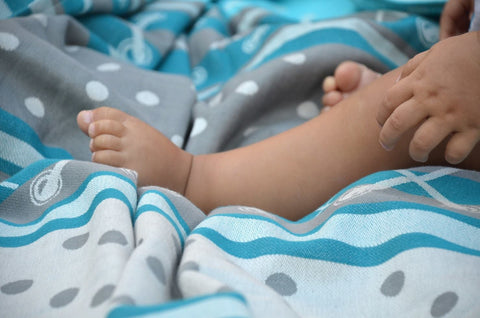 Close-up of a child's legs and feet wrapped in a blue and gray patterned blanket.