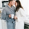 Man and woman embracing while holding coffee mugs and wearing robes