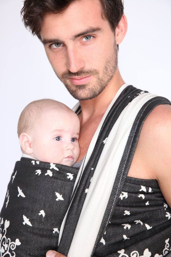 Man babywearing in a black wrap with white birds and wunderland design
