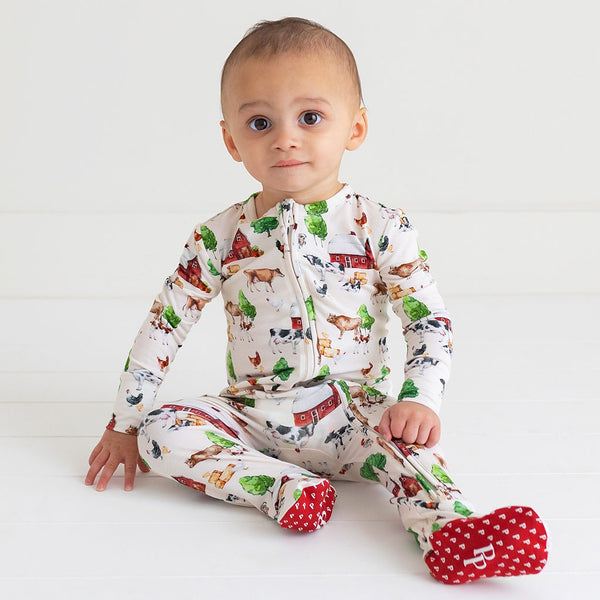 Toddler sitting in a zippered footie. Country farm print on a cream background. 