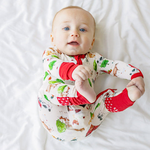 Baby lying down in onepiece. Country farm print on a cream background. Zipper, wrists and foot cuffs are red.