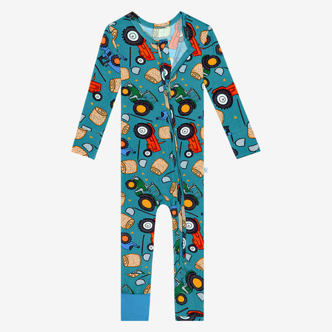 Zipper convertible one piece. Convertible cuffs are solid blue. Pattern of cartoonish red and green tractors, bails of hay and farm tools are on a blue background. 