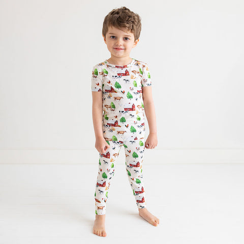Boy standing in short sleeve long pants pajama set. Country farm print on a cream background.