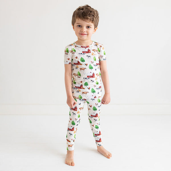 Boy standing in short sleeve long pants pajama set. Country farm print on a cream background.