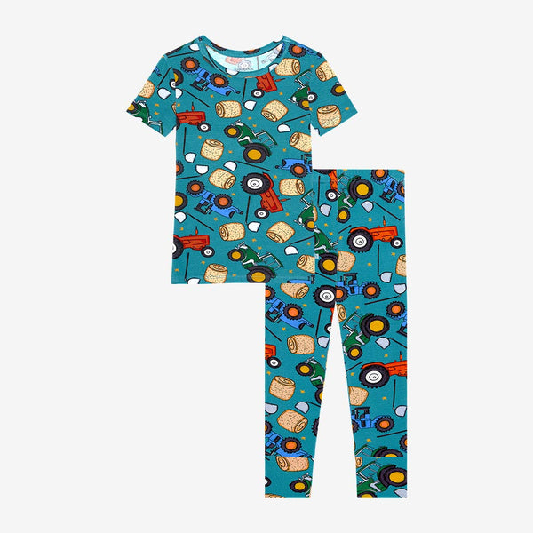 Pajama set with short sleeves and long pants. Pattern of cartoonish red and green tractors, bails of hay and farm tools are on a blue background.