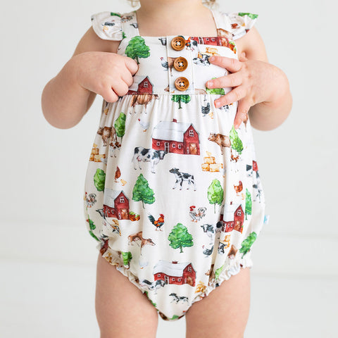 Toddler girl standing in bubble romper. Country farm print on a cream background.