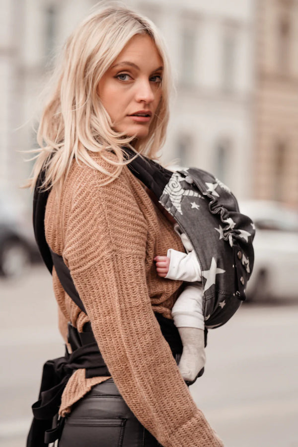 Woman in jeans wearing a babycarrier. Carrier is black with white large stars.