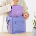 Woman putting an omiebox lunch box into Lavender lunch tote with shoulder strap. The tote has lilac trim around the edges.